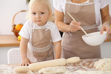 Little girl and her blonde mom in beige aprons  playing and laughing while kneading the dough in the kitchen. Homemade pastry for bread, pizza or bake cookies
