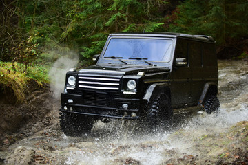 SUV or offroad car in black color crossing water stream Car racing with creek on way. Offroad race in forest Extreme driving, challenge and 4x4 vehicle concept © Volodymyr