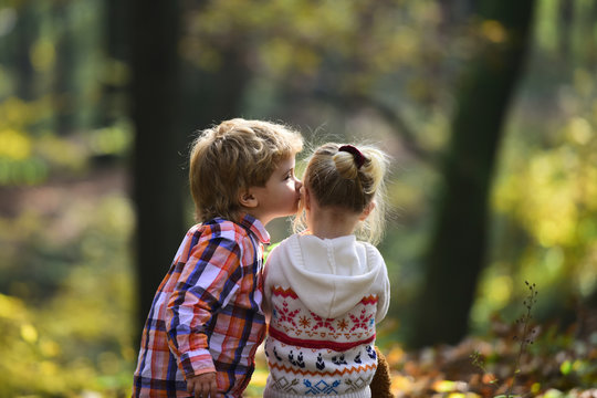 Little boy kiss small girl friend in autumn forest. Brother kiss sister with love in woods. Valentines day concept. Family love and trust. Childhood friendship and children early development