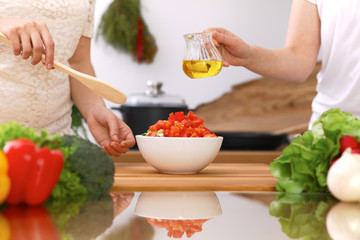 Closeup of human hands cooking in kitchen. Mother and daughter or two female friends cutting vegetables for fresh salad. Healthy meal, vegetarian food and lifestyle concepts