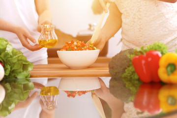 Closeup of human hands cooking in kitchen. Mother and daughter or two female friends cutting vegetables for fresh salad. Healthy meal, vegetarian food and lifestyle concepts