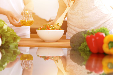 Closeup of human hands cooking in kitchen. Mother and daughter or two female friends cutting vegetables for fresh salad. Healthy meal, vegetarian food and lifestyle concepts