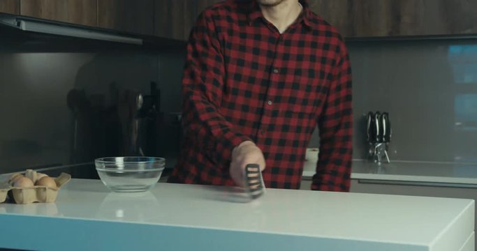 Funny hipster man goofing around with a spatula in the kitchen