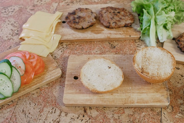 Products for preparation of burgers: buns, tomatoes, cucumbers, cutlets, cheese, salad, sauce, bacon on the table. Top view.