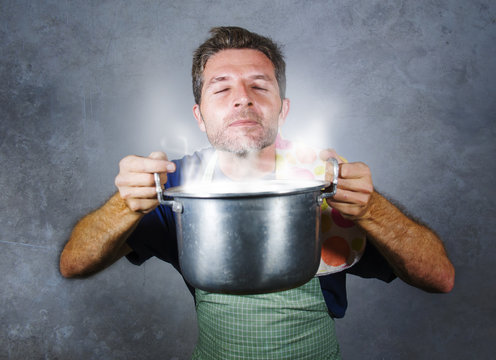 Young Attractive Happy And Proud Home Cook Man Cooking Soup Holding Kitchen Pot Smelling The Meal Aroma Gesturing Delighted And Satisfied