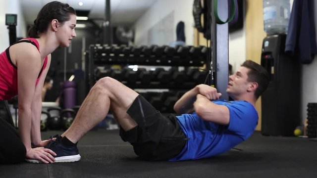 Man In Gym Doing Sit Ups Encouraged By Personal Trainer