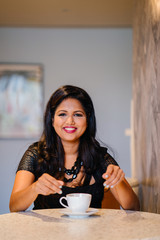 Portrait of a youthful but confident and mature Indian woman having a cup of coffee while patiently...