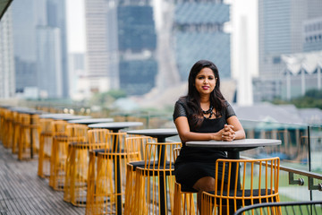 A charming desi woman is seated in a row of tables and yellow chairs. She is enjoying quiet time alone in the afternoon.