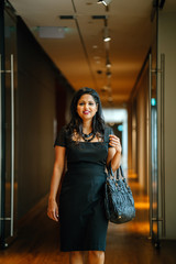 A confident young Indian Asian lady is walking through the hallways of their office after a long day's work. She looks relieved that another day at the office is over.