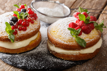 Two small Victoria cake decorated with black and red currants, raspberries and mint close-up....