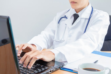 Young male in Uniform of doctor using digital technology laptop for Output Device on the office desk.