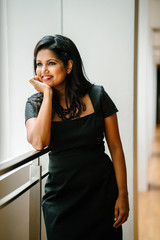 An Indian Asian female professional is standing in the hallway during the day. She is smiling with confidence as she flaunts her elegant dress.