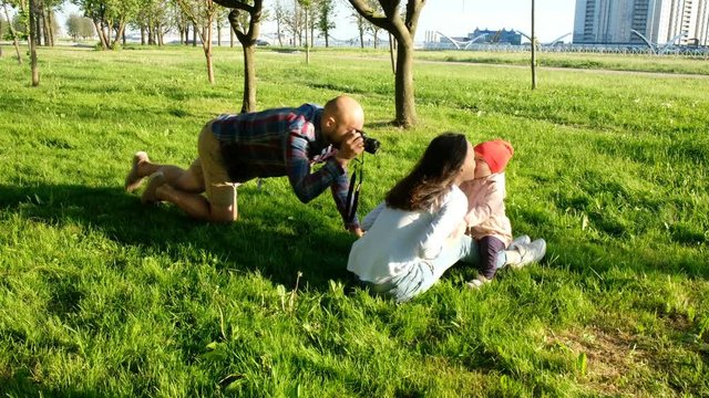 Young father photographing kissing mother and daughter in the park at sunset. Happy family taking photos in nature
