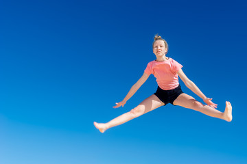 Obraz premium ein junges Mädchen springt vor blauem Himmel im Spagat hoch in die Luft