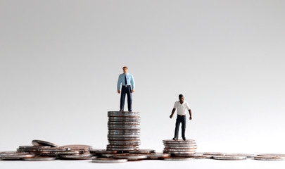 Racial wage gap concept. Miniature people standing on a pile of coins. - obrazy, fototapety, plakaty