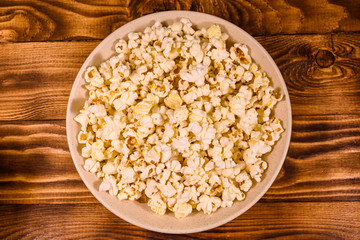 Ceramic plate with popcorn on wooden table. Top view