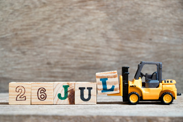 Toy forklift hold block l to complete word 26 jul on wood background (Concept for calendar date in month July)