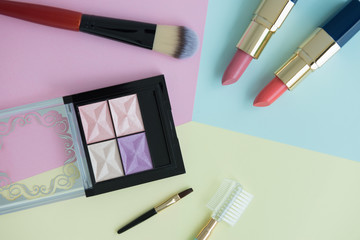 Flat lay creative concept of female decorative cosmetic for orange and pink lipstick, cheek brush, lipstick palette and eyeshadow palette on the colorful background with copy space