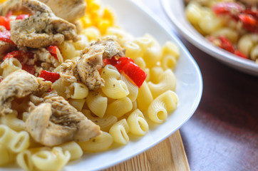 Hot Pasta with Chicken Breast Meat and Vegetables in Large White Plate on Wood Table, Close-Up. Food Background