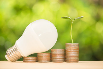 LED bulb on the growing coin stack with warm light and green nature background for saving energy concept