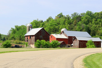 Fototapeta na wymiar Agriculture and farming background. Rural life concept.Scenic countryside spring landscape with rural road along farm buildings and ted barns on a woods background. Midwest USA,Wisconsin,Madison area.