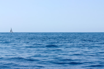 Obraz premium Sea water landscape with dark waves and a lonely white yacht at the horizon on sunny day.