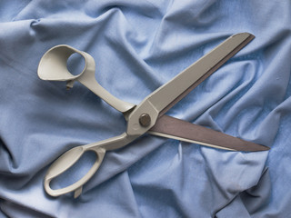 Open pair of scissors with a gray handle on blue background