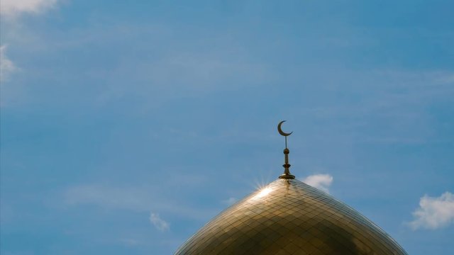 A golden minaret with the symbol of Islam - a crescent with a sunlight flare against the blue sky with clouds. TimeLapse.