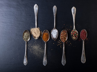 Old metal spoons with different kind of spices on a black background