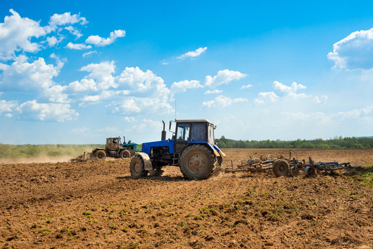 Two tractors with a plow in a field on a sunny day. Preparing land for sowing. Agricultural works at farmlands. Agriculture industry