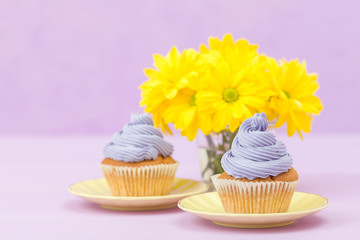 Cupcakes decorated with violet cream and bouquet of yellow chrysanthemums on violet pastel background with text area for greeting banner.