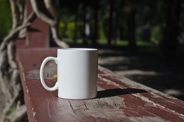 A blank white mug on the wooden bench of a park. 