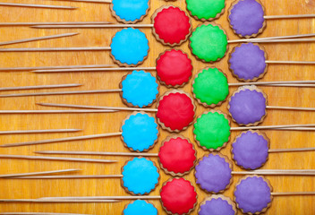 Gingerbread cookies with colored mastic on sticks on the old wooden cutting board