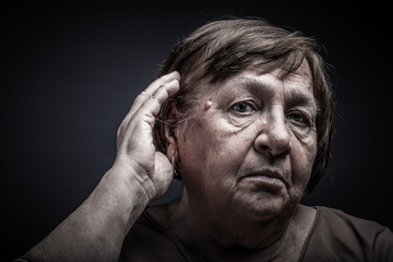 Studio portrait of elderly woman. Listens or corrects hair. Toned