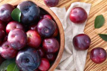 Bowl with ripe juicy plums on wooden table