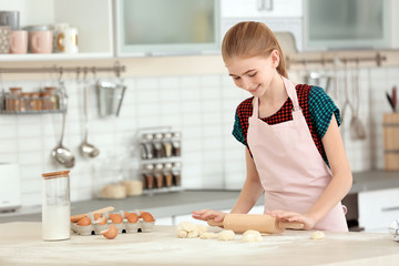 Teenage girl rolling dough on table in kitchen