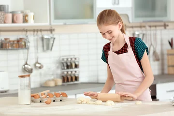 Selbstklebende Fototapeten Teenage girl rolling dough on table in kitchen © New Africa