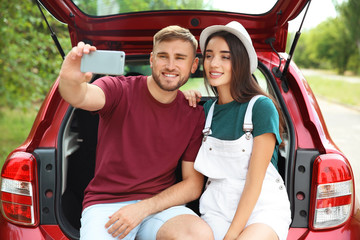 Fototapeta na wymiar Beautiful young couple taking selfie in car trunk