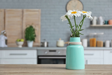 Vase with flowers and blurred view of kitchen interior on background