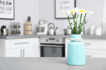 Vase with flowers and blurred view of kitchen interior on background