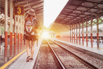Young girl traveler with backpack bag walking on platform beside railroad 