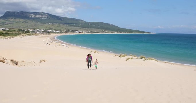 four years old blonde girl with woman mother with backpack walking on sand dune at Beach Bolonia in Tarifa, Cadiz, Andalusia, Spain
