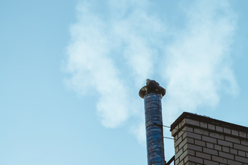 Dove on chimney above bright blue sky in cloud of steam or smoke with copy space. Small pigeon bask on pipe. Beautiful background from clear heaven above roof with silhouette of bird on pipe.