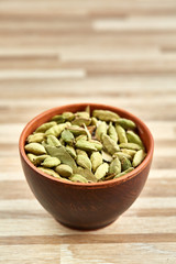 Green cardamon in ceramic bowl on textured wooden background close-up, top view, selective focus, vertical.