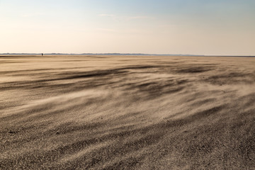 Fototapeta na wymiar Strand von Spiekeroog bei Starkwind im Winter mit einsamer Person am Horizont
