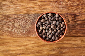 Clay bowl with dried allspice berries on vintage wooden background, top view, close-up, macro, selective focus.