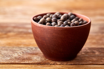 Close-up of clay bowl with dried allspice berries on vintage wooden background, macro, shallow depth of field.