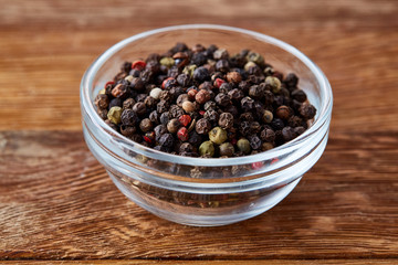 Front view of peppercorn in glass bowl on wooden background, close-up, selctive focus.