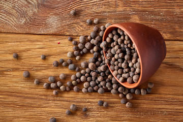 Overturned clay bowl with dried allspice berries on rustic wooden background, close-up, macro, selective focus.