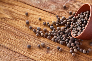Close-up of overturned clay bowl with dried allspice berries on rustic wooden background, macro, shallow depth of field.